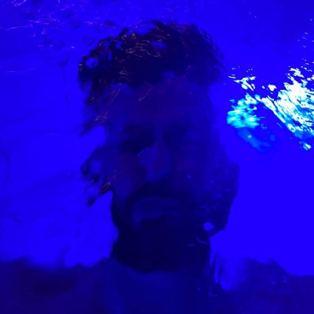 Samuel La Manna immerso in acqua illuminata di blu, atmosfera surreale